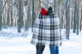 Guy and girl in knitted hats with buboes standing in winter in park are covered with warm blanket. Back view Royalty Free Stock Photo