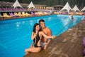 Guy and girl posing against the swimming pool with perfect aqua water and taking selfie photo with monopod on the resort Royalty Free Stock Photo