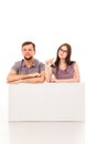 A guy and a girl are posing with a white sign, cardboard, a sign in their hands.