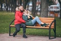 A guy and a girl are resting on a bench in an autumn park. A loving couple in jackets sits on a bench in the main park Royalty Free Stock Photo