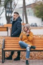 A guy and a girl are resting on a bench in an autumn park. A loving couple in jackets sits on a bench in the main park Royalty Free Stock Photo