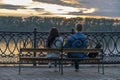 A guy and a girl sitting on a bench on the waterfront and watching the beautiful sunset