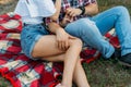 a guy and a girl are sitting on a plaid veil on the grass, hugging and kissing. a man in a plaid shirt and jeans, with a watch on Royalty Free Stock Photo