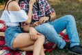 A guy and a girl are sitting on a plaid veil on the grass, huggingholding hands. the man put his hand on the girl`s foot. a man i Royalty Free Stock Photo