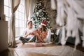 Guy and girl in white t-shirts and Santa Claus hats sit with red cups on the floor in front of the window next to the Royalty Free Stock Photo