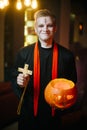 Guy in a Halloween priest costume holds a carved pumpkin in his hand and smiles