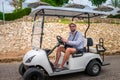 A guy in a hat and glasses rides a golf cart on an Arab street. A man sits behind the wheel of an electric car in a tropical Royalty Free Stock Photo