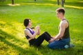 guy helps the girl to do the press exercise, sitting on the lawn in the park