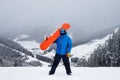 The guy hold on the shoulder orange snowboard in winter