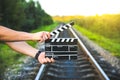 Guy is holding black clapperboard in hands. Man is directing and filming some amateur cinema movie. Rail trails on the background