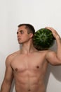 The guy is holding a huge watermelon on his shoulder. A guy with a bare torso on a light background