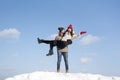 Guy holds girl in his arms on snow-covered hill against blue sky. Winter sunny day in mountance Royalty Free Stock Photo