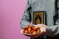 The guy holds the Holy Quran, Islamic rosary and dates. On a pink background. Royalty Free Stock Photo