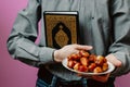 The guy holds the Holy Quran, Islamic rosary and dates. On a pink background. Royalty Free Stock Photo