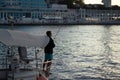 Guy with the hook is fishing on the coast of the port resort town, sea city at evening