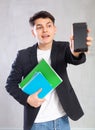 Guy in jacket with stack of notebooks shows empty mobile phone screen.Device close up unfocused