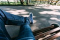 The guy in jeans and sneakers sits on a wooden bench in the park. First-person view