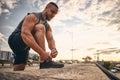 The guy lifted and bent his knee to tie the lace on the sneaker while jogging against the backdrop of the city and sunrise. Sport