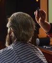 Guy with long dyed blond hair close up. Do not cut your own hair. Barber works on hairstyle for bearded man barbershop