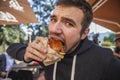 A guy is looking at the camera with the eyes full of dissapointment. He is eating his hamburger. Bad taste concept Royalty Free Stock Photo