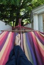 Guy lying down in a colorful Hammock resting barefoot.Crossed legs of a man taking nap in blue hippie pants in a summer garden of