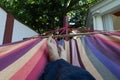 Guy lying down in a colorful Hammock resting barefoot.Crossed legs of a man taking nap in blue hippie pants in a summer garden of