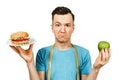 Guy with measuring tape holds a burger and green apple. Concept of choosing between healthy and unhealthy foods Royalty Free Stock Photo