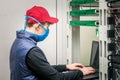 A guy in medical mask is working in front of a laptop. Programmer in virus protection tools works in the server room datacenter. Royalty Free Stock Photo