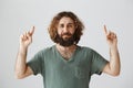 Guy is not sure that he likes what he sees. Portrait of attractive arabian with long curly hair and beard pointing up