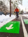 A guy in an orange jacket rides a bicycle along a bike path in winter