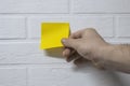 The guy peels off the yellow sticker for notes on the background of a white brick wall. Royalty Free Stock Photo