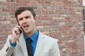 Guy on the phone with headache. Upset unhappy male talking on phone on brick wall background. Negative human emotions Royalty Free Stock Photo