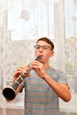 The guy plays the clarinet at home near the window. Doing home music assignment