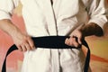 Guy poses in white kimono with black belt, close up. Karate fighter with fit strong hands gets ready to fight.