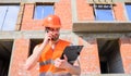 Guy protective helmet stand in front of building made out of red bricks. Builder vest and helmet works at construction