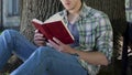 Guy reading gripping book under tree, engrossed into plot, avid book reader