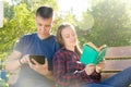 Guy reads book on the tablet next to the sitting girl reads book in summer sunny day in park Royalty Free Stock Photo