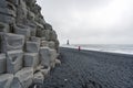 Guy with red jacket are walking on black beach of Reynisfjara in Iceland during windy and overcast day. Basalt rocks infront Royalty Free Stock Photo