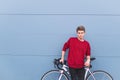 Guy in a red sweatshirt standing with a white bike on the background of a blue wall and looking into the camera Royalty Free Stock Photo