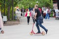 Guy roll on a scooters pushing off a road around square in the park for walks and rest among the other people on a spring day