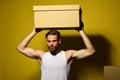 Guy with sexy torso holds box above head. Royalty Free Stock Photo