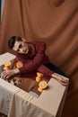 A guy in a shirt sits at a table with a mirror and orange oranges fabric background studio model Royalty Free Stock Photo