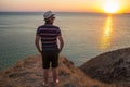 A guy in shorts and straw hat standing on a cliff by the sea