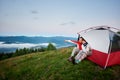 Guy shows his hand in distance sitting at tent near girl from against Carpathian mountains Royalty Free Stock Photo