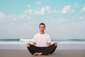 The guy sits on the seashore in the lotus position and meditates.