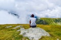 The guy sits on a stone surrounded by fog and low clouds near Transalpina road in Romania Royalty Free Stock Photo