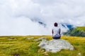 The guy sits on a stone surrounded by fog and low clouds near Transalpina road in Romania Royalty Free Stock Photo