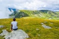 The guy sits on a stone surrounded by fog and low clouds near Transalpina road in Romania Royalty Free Stock Photo