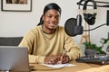 Guy sitting by workplace with microphone, headphones, soundboard and laptop