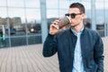 The guy in stylish sunglasses, a man walks around the city and drinking coffee from a paper Cup, a handsome guy walks around and r Royalty Free Stock Photo